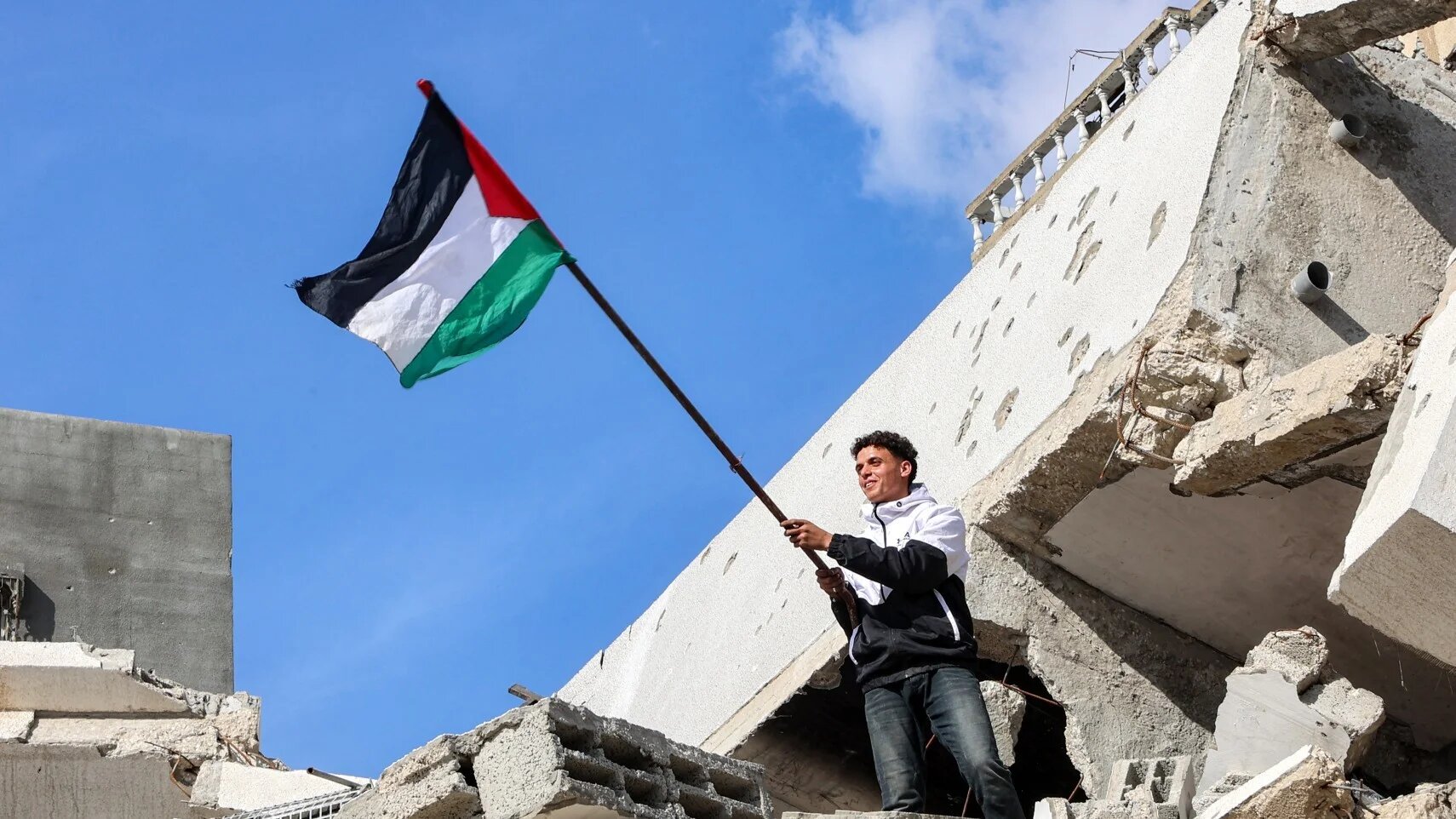 A Palestinian holds the national flag atop the rubble of a collapsed building in the northern Gaza on 19 January, 2025 after a ceasefire deal in the war between Israel and Hamas-afp.jpg